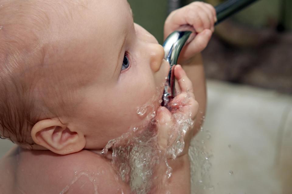 Bathing baby drinking clean water from kitchen tap.