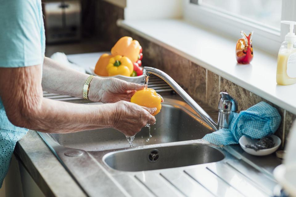Woman in the kitchen washing yellow peppers over the sink