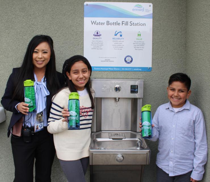 Three people holding water bottles at a water fill station.
