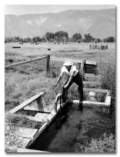 Farmland irrigation canal with farmer opening gate to divert water.