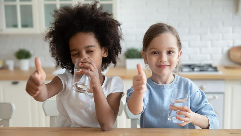 Two children in the kitchen, smiling and drinking water
